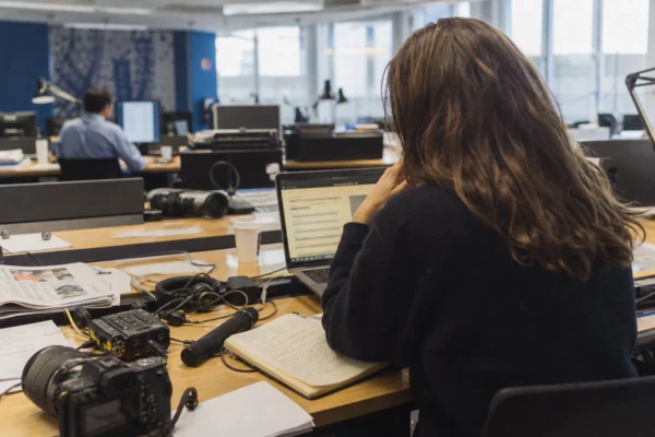 Journaliste en rédaction préparant un sujet sur les nominations politiques, avec carnet, micro et écran flou