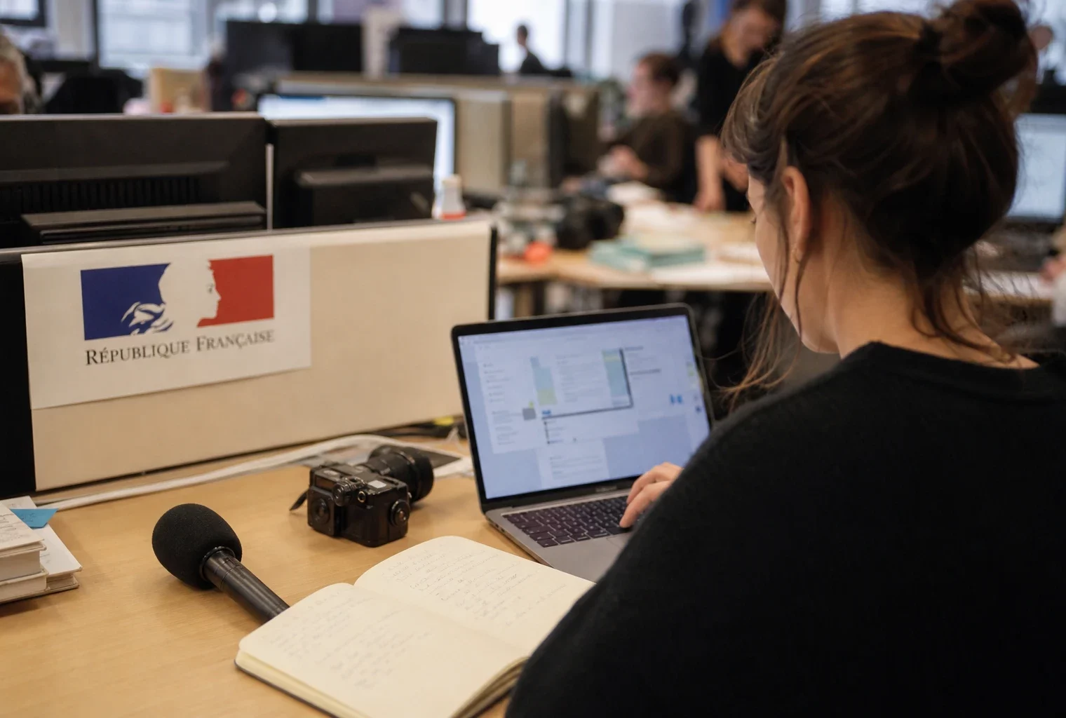 Journaliste en rédaction préparant un sujet politique avec micro, carnet et écrans flous dans une ambiance lumineuse