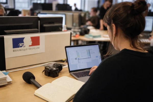 Journaliste en rédaction préparant un sujet politique avec micro, carnet et écrans flous dans une ambiance lumineuse