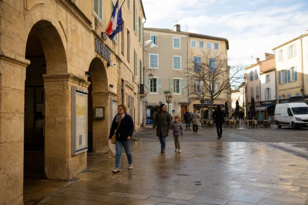 Scène de rue française devant une mairie, avec passants anonymes et ambiance calme de ville moyenne.