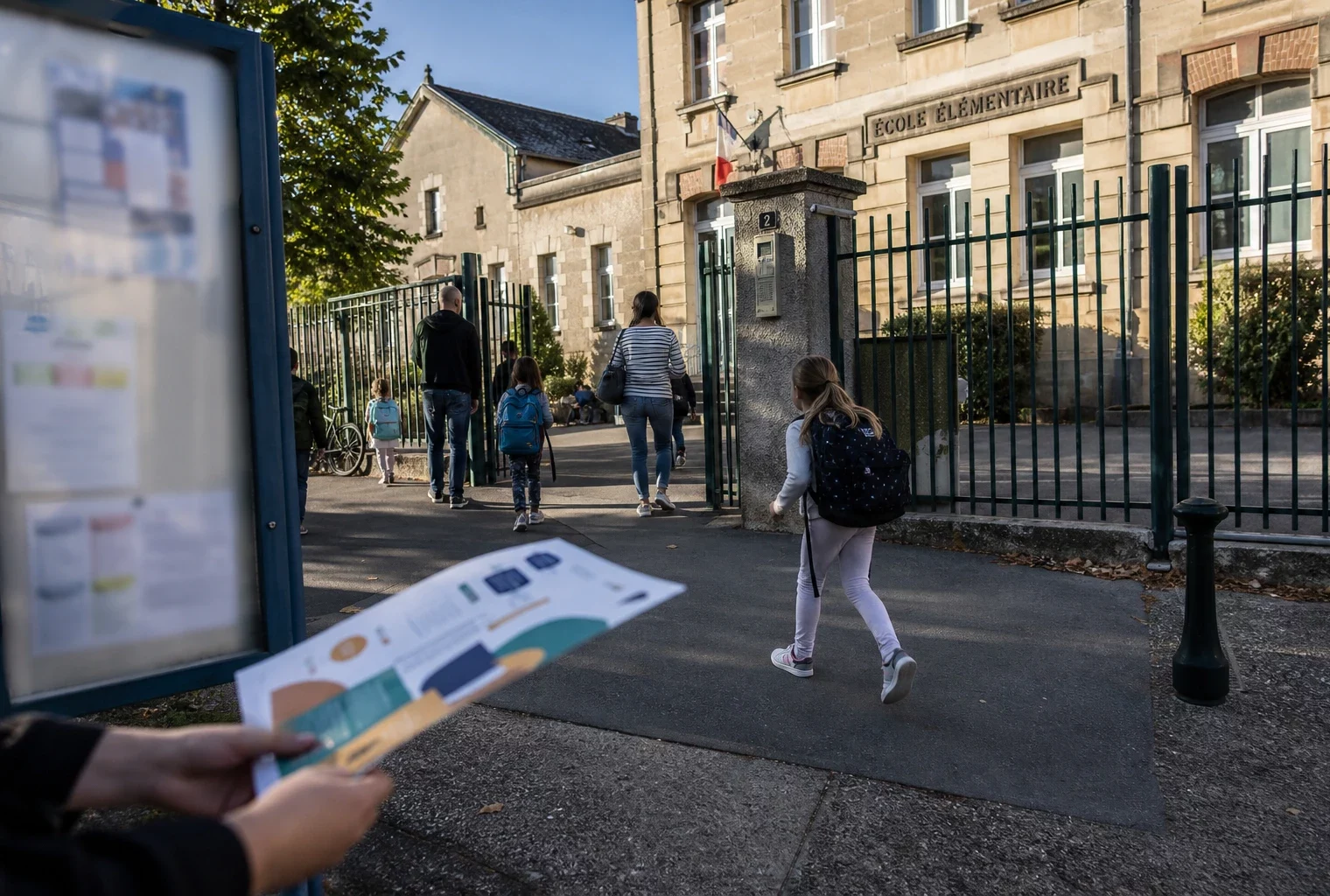 Parents et élèves arrivent devant une école de ville moyenne française par temps clair, en scène de reportage.
