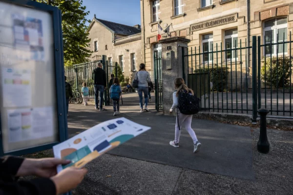 Parents et élèves arrivent devant une école de ville moyenne française par temps clair, en scène de reportage.