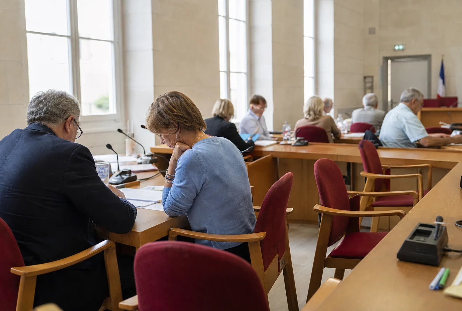Salle municipale lumineuse avec micros, dossiers et chaise vide, ambiance de résultats du bac