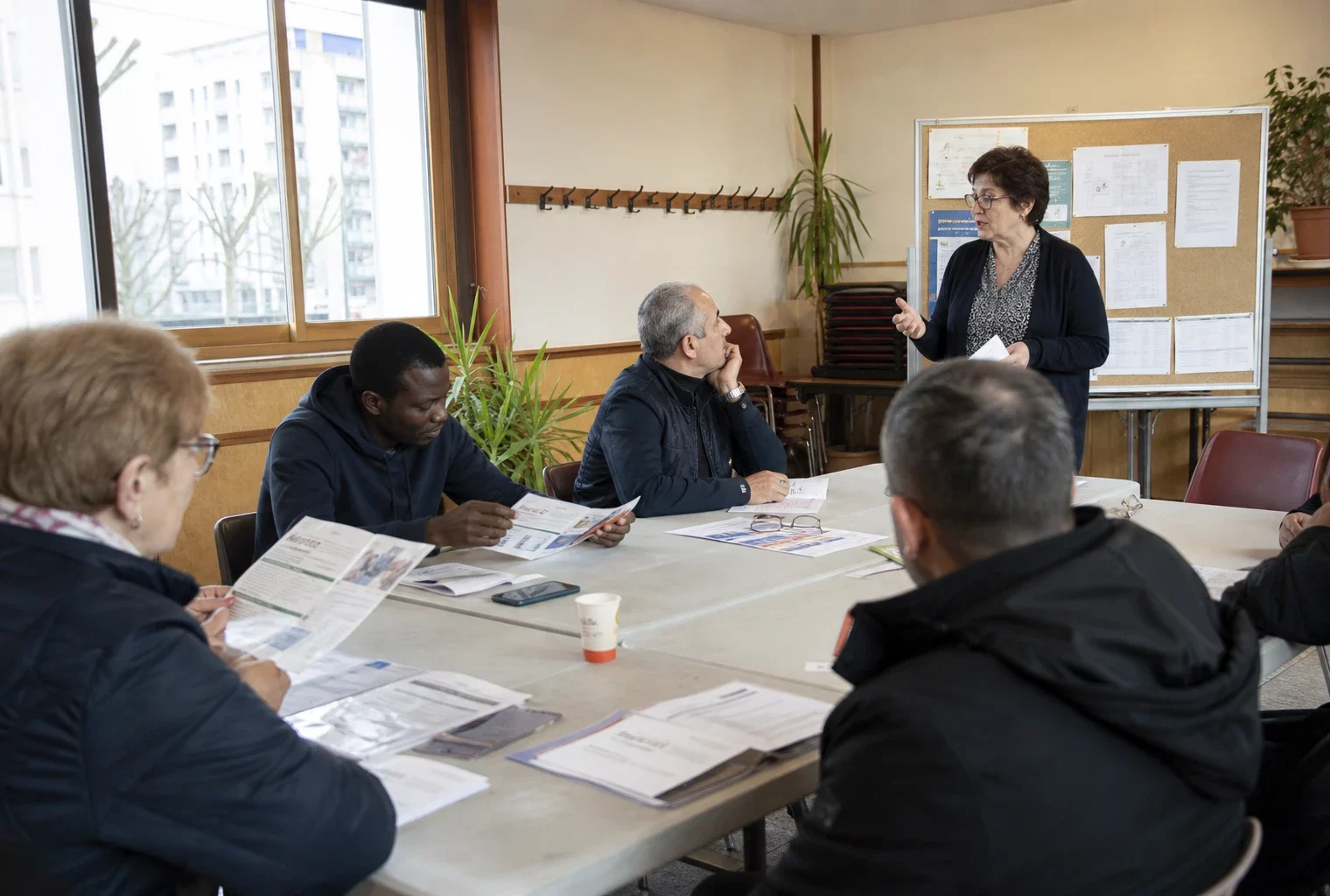 Réunion de quartier dans une salle associative lumineuse avec des habitants anonymes autour de tables