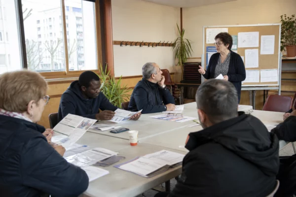 Réunion de quartier dans une salle associative lumineuse avec des habitants anonymes autour de tables