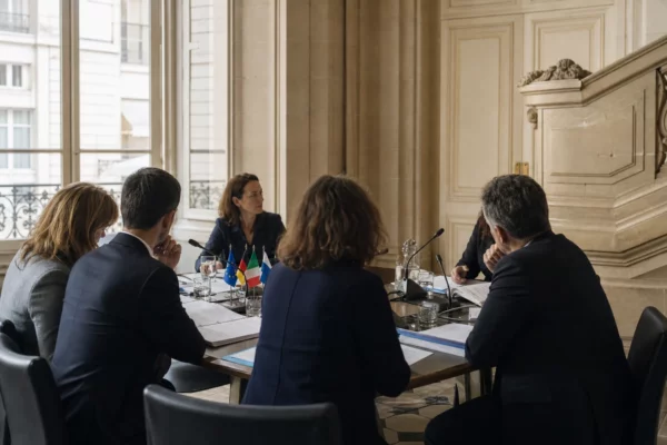 Réunion européenne sobre avec dossiers, micros et silhouettes de dos dans une salle institutionnelle claire.