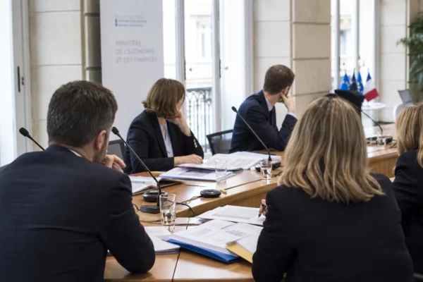 Réunion européenne sobre avec dossiers, micros et silhouettes de dos dans une salle claire