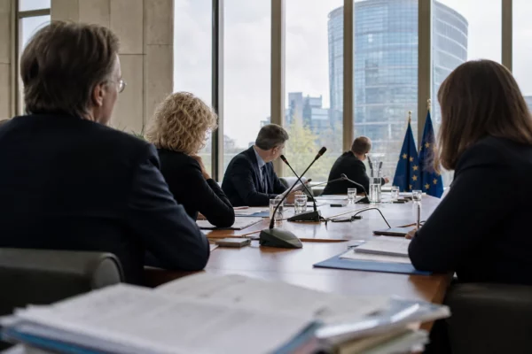 Réunion européenne sobre à Strasbourg avec cinq silhouettes anonymes, dossiers ouverts et micros de table.