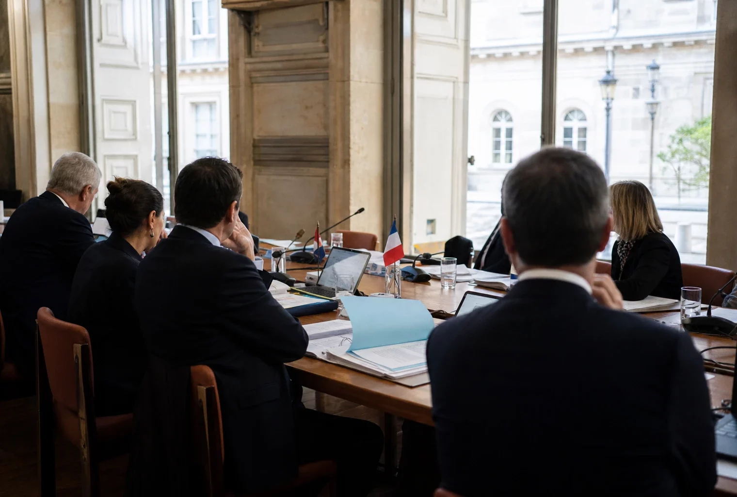 Réunion institutionnelle européenne avec dossiers, micros et silhouettes anonymes dans une salle claire