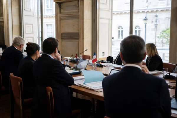 Réunion institutionnelle européenne avec dossiers, micros et silhouettes anonymes dans une salle claire