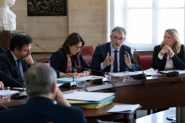 Députés anonymes réunis dans une salle de commission de l’Assemblée nationale, avec micros et dossiers ouverts.