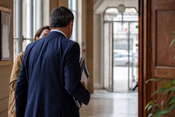 Un élu local anonyme dans un hall de mairie, dossier en main, lumière naturelle et arrière-plan urbain flou.