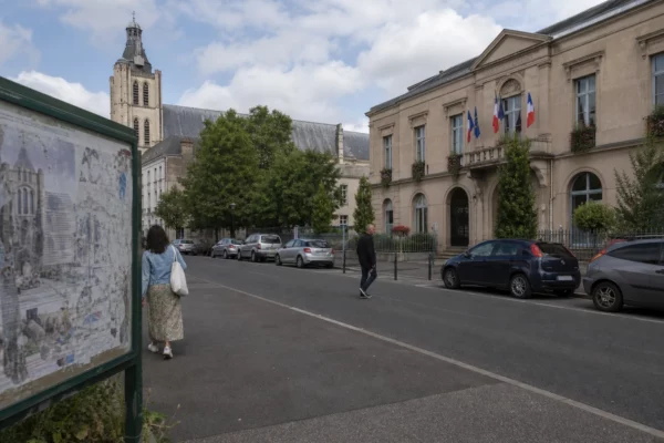 Rue de Saint-Denis près de la mairie, avec passants anonymes et un rappel discret du chantier de la basilique.