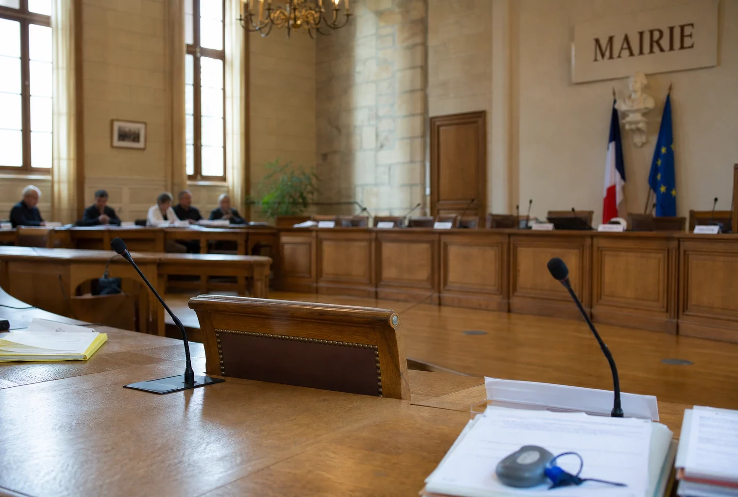 Salle de conseil municipal lumineuse avec chaise vide, micros et dossiers, ambiance politique locale sobre