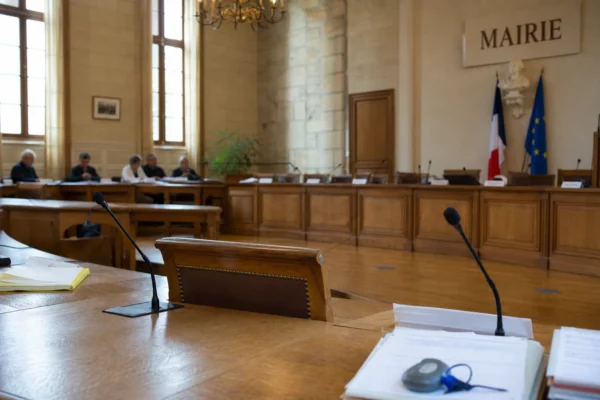 Salle de conseil municipal lumineuse avec chaise vide, micros et dossiers, ambiance politique locale sobre