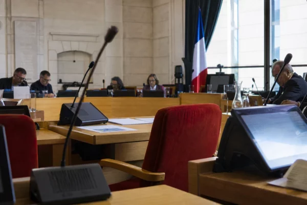 Salle du conseil municipal de Perpignan avec chaises vides, micros et dossiers flous, dans une lumière naturelle claire.