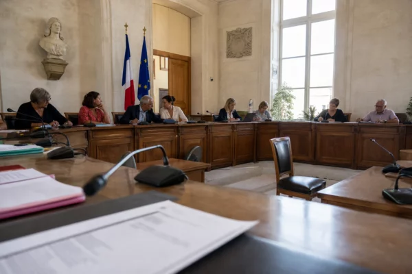 Salle municipale française avec chaise vide, micros et dossiers flous dans une scène institutionnelle calme