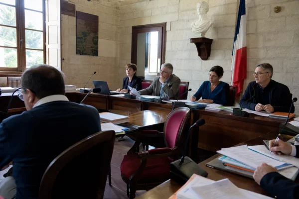 Salle municipale de conseil local avec chaise vide, micros et dossiers flous dans une lumière naturelle claire.