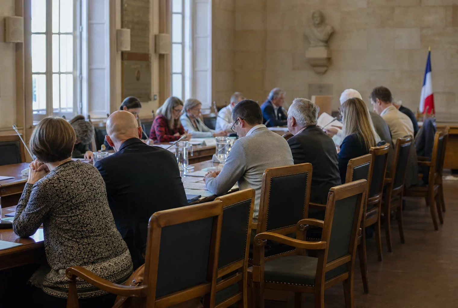 Salle municipale avec micros, dossiers et chaise vide pendant un débat politique sur la canicule.