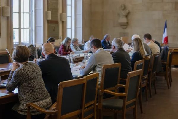 Salle municipale avec micros, dossiers et chaise vide pendant un débat politique sur la canicule.