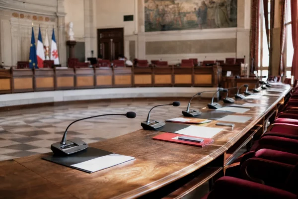 Salle municipale de Nice avec micros, dossiers ouverts et chaise vide, dans une ambiance de commémoration discrète.