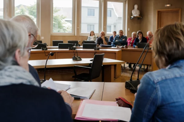 Salle municipale française avec chaise vide, micros et dossiers flous lors d’une réunion locale.