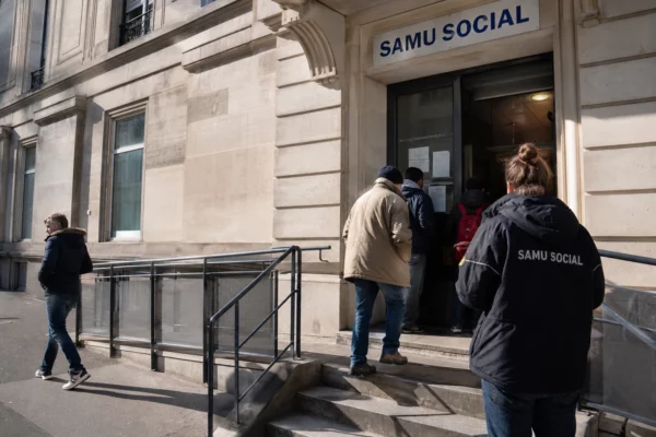 Façade institutionnelle du Samu social à Paris, avec des personnes anonymes à l’entrée sous une lumière naturelle claire.