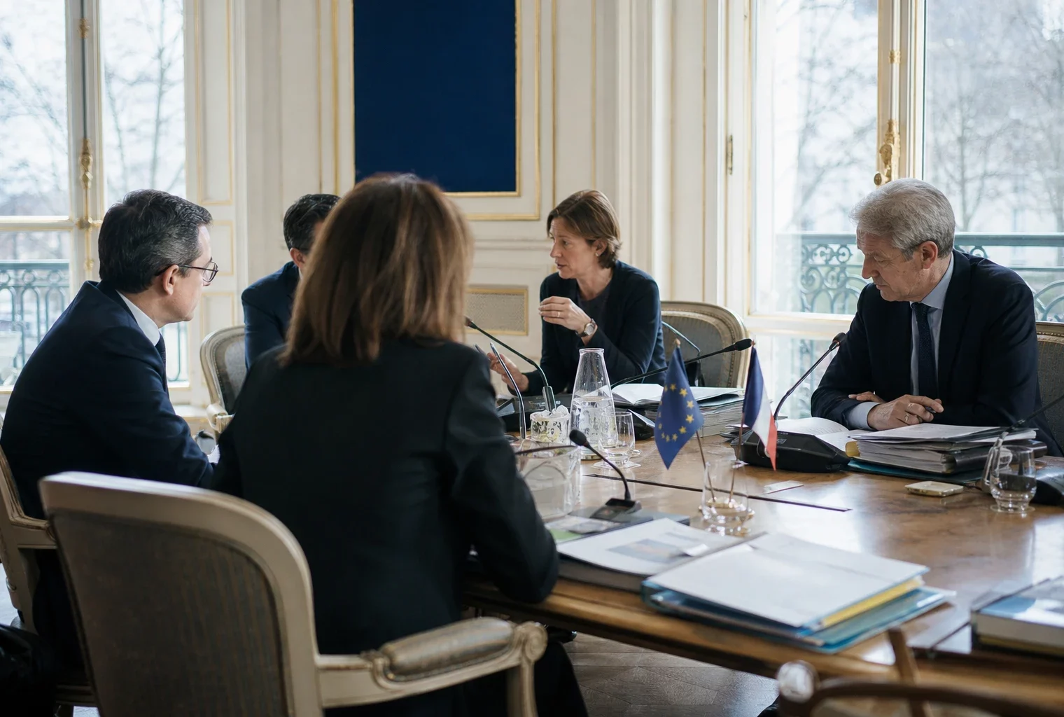 Réunion européenne sobre avec plusieurs officiels autour d’une table, dossiers ouverts et drapeaux discrets en arrière-plan.