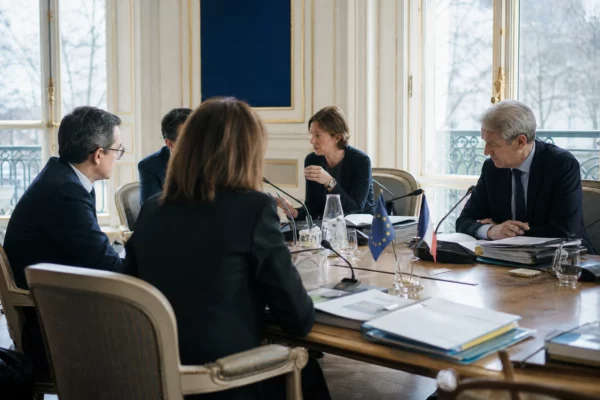 Réunion européenne sobre avec plusieurs officiels autour d’une table, dossiers ouverts et drapeaux discrets en arrière-plan.