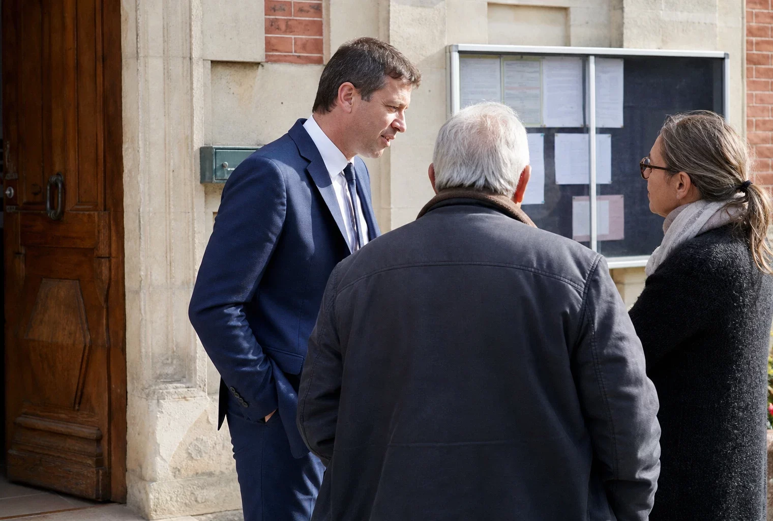Des habitants discutent devant une mairie de village, dans une scène civique française claire et naturelle.