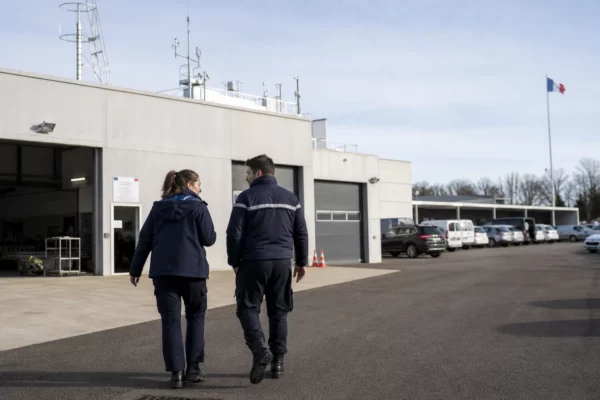 Scène calme dans un site français de sécurité, avec silhouettes anonymes et matériel de terrain en extérieur.