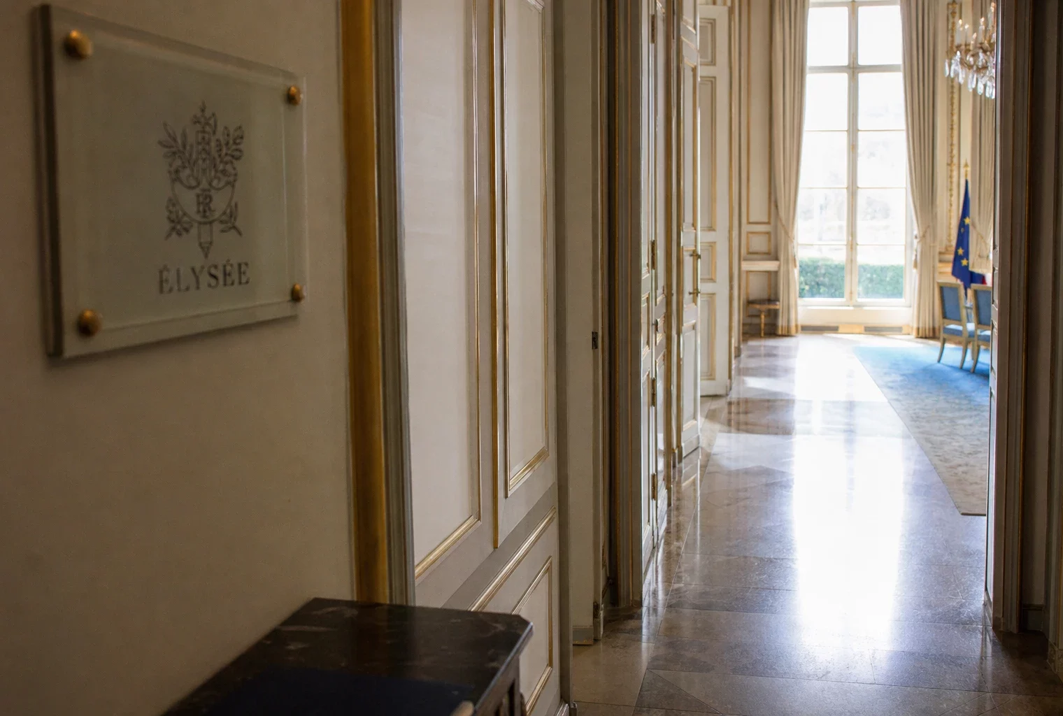 Couloir vide de l’Élysée avec marbre clair, dorures et lumière naturelle, en vue oblique de reportage.