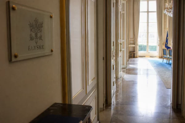 Couloir vide de l’Élysée avec marbre clair, dorures et lumière naturelle, en vue oblique de reportage.
