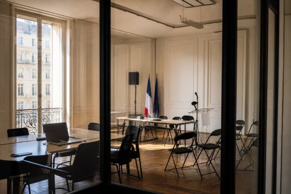 Intérieur clair d’un siège politique parisien vide, avec table de réunion, micros et lumière naturelle latérale.