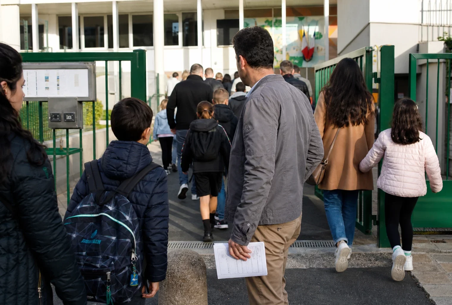Parents et enfants à l’entrée d’une école publique française, scène de vie citoyenne en lumière naturelle.