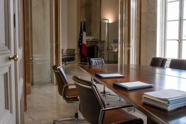 Salle institutionnelle vide dans un siège politique parisien, avec table de réunion, dossiers fermés et lumière naturelle claire.