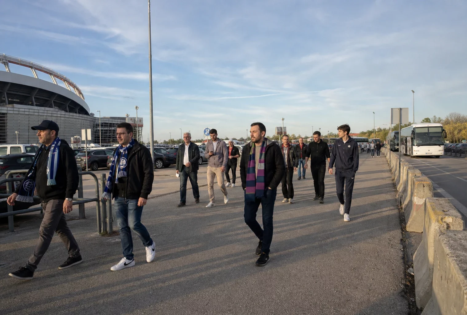 Des supporters européens marchent vers le stade sur un large accès piéton, dans une scène de reportage claire et réaliste.