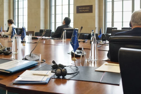 Table de négociation européenne avec dossiers, casques et drapeaux miniatures, dans une salle institutionnelle lumineuse