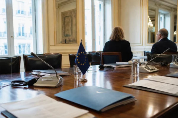 Table diplomatique européenne avec dossiers, casques d’écoute et petits drapeaux discrets dans une salle de réunion.