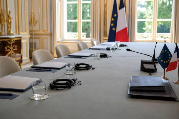 Table de négociation européenne avec dossiers, casques et verres d’eau dans une salle institutionnelle lumineuse
