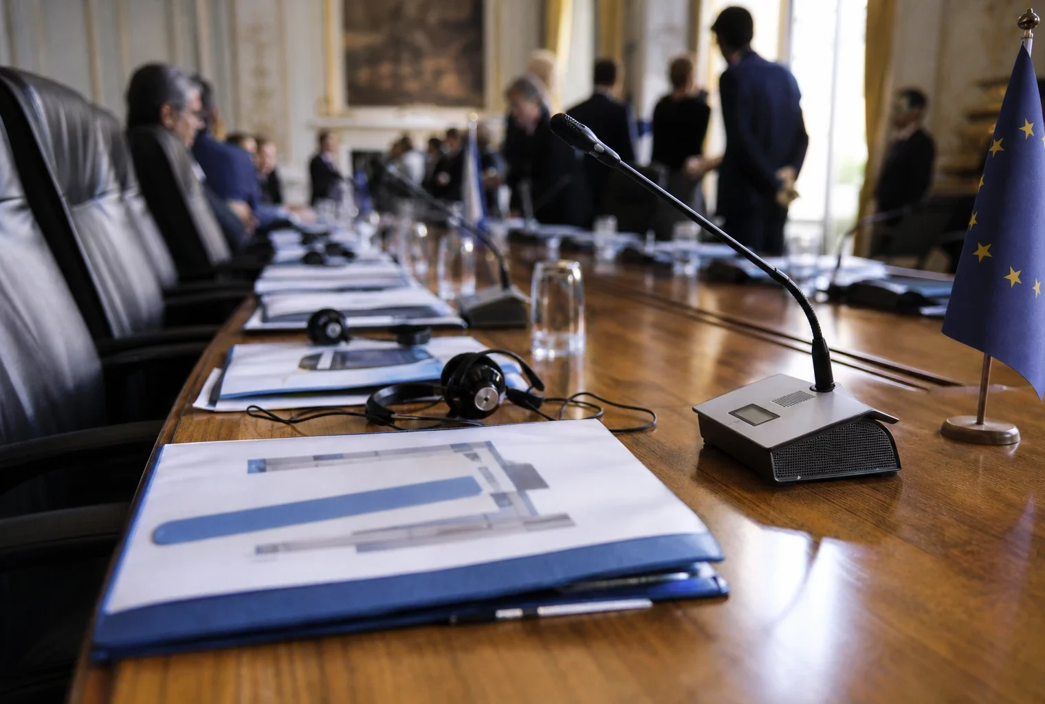 Table diplomatique européenne avec dossiers, écouteurs et drapeaux miniatures discrets avant un briefing sportif