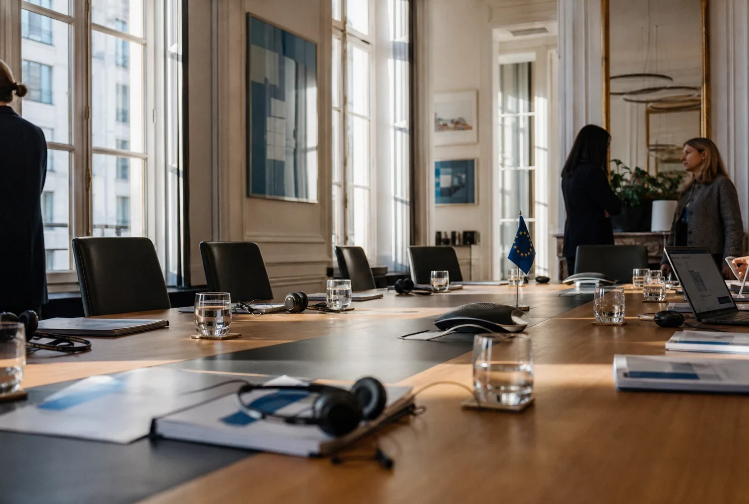 Table de négociation européenne avec dossiers, casques audio et petits drapeaux de table dans une salle institutionnelle lumineuse.