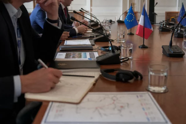 Table de négociation internationale avec dossiers, micros et petits drapeaux, dans une salle claire et réaliste.