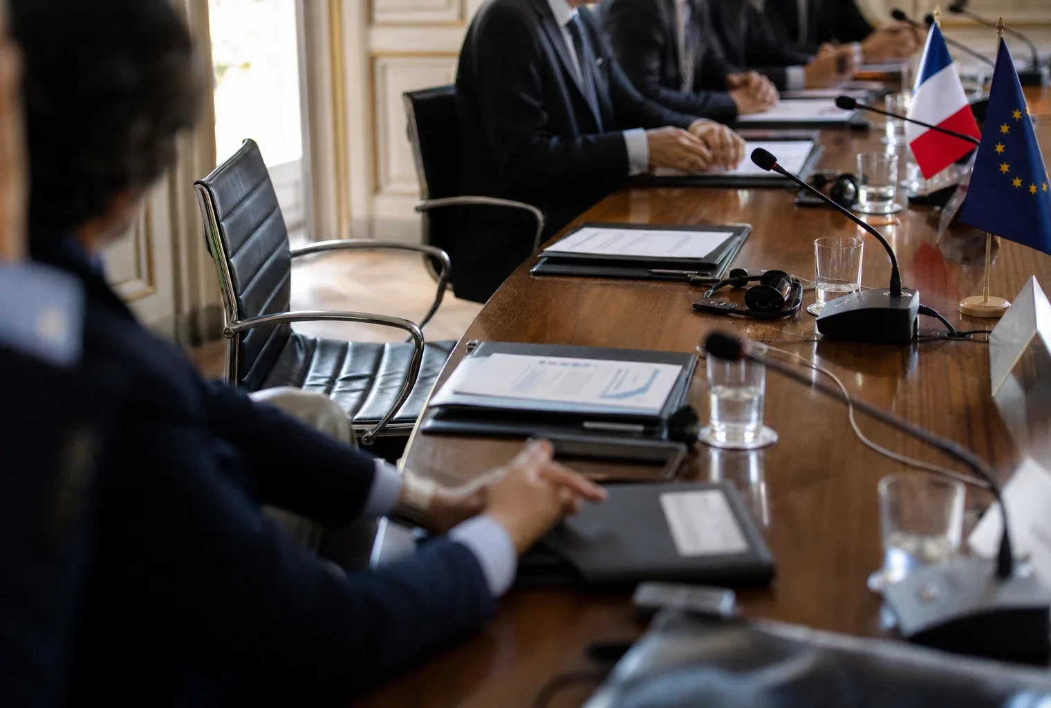 Table de négociation avec micros, dossiers fermés et silhouettes anonymes dans une salle lumineuse
