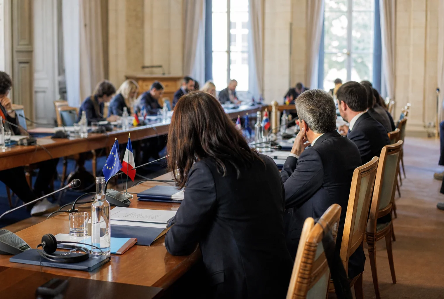 Réunion diplomatique avec dossiers, micros et casques de traduction autour d’une table de négociation lumineuse.