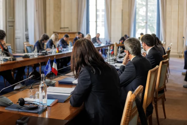 Réunion diplomatique avec dossiers, micros et casques de traduction autour d’une table de négociation lumineuse.