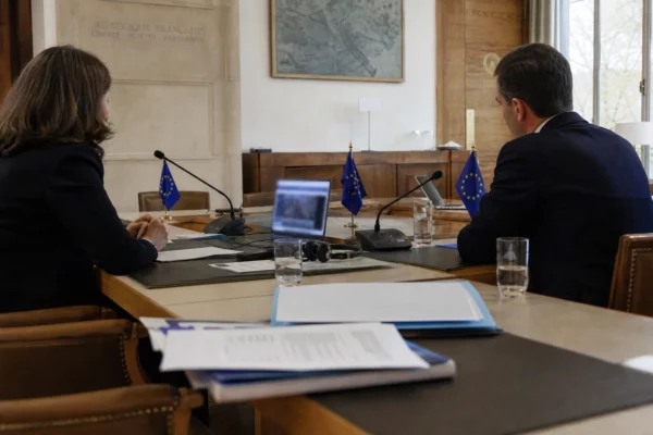 Table de négociation institutionnelle avec micros, dossiers fermés, écouteurs et silhouettes anonymes dans une salle claire.