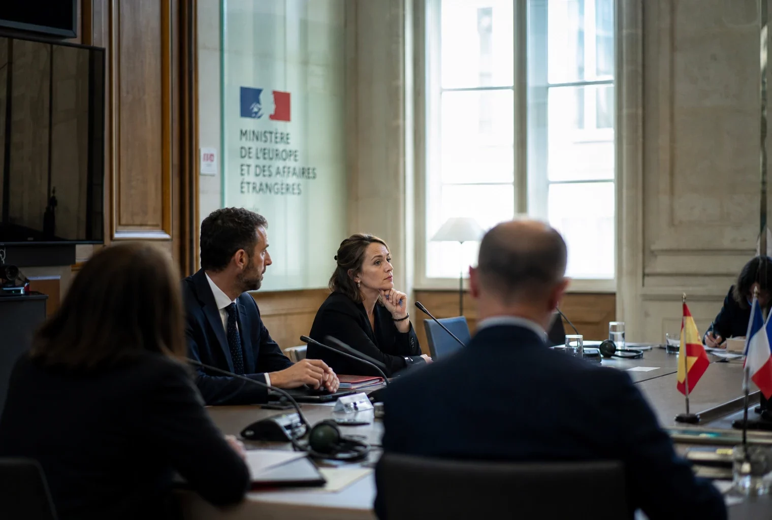 Table de négociation internationale à Paris avec micros, dossiers fermés et silhouettes anonymes sous une lumière claire.