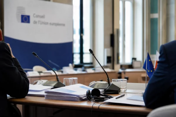 Table de négociation européenne avec dossiers, casques et petits drapeaux, dans une salle institutionnelle lumineuse.
