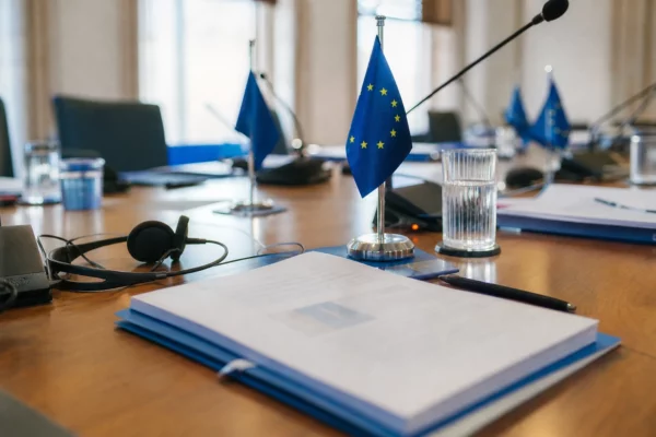 Table de négociation européenne avec dossiers, écouteurs, verres d’eau et drapeaux miniatures discrets.